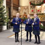 three young girls in Eaton Square uniform singing into a microphone in Church at Christmas concert