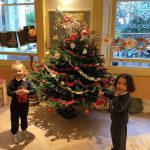 two nursery children standing in front of a christmas tree