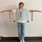 girl holding arms out with medals hanging off