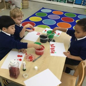 3 children are painting poppies onto the sheet of paper in front of them