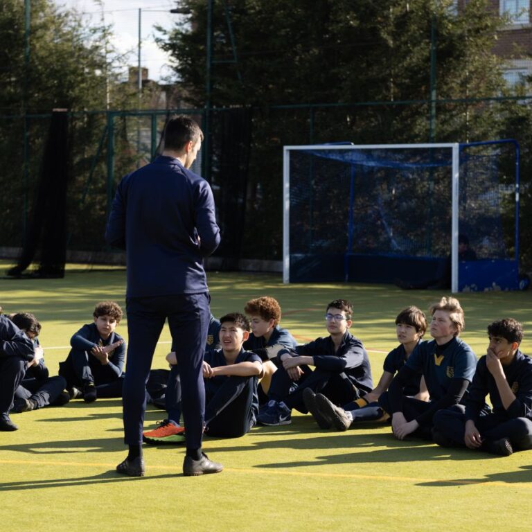 Sports teacher talking to students on the astroturf before a game of football